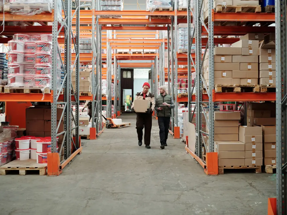 Two warehouse staff walking between shelves, one with a tablet